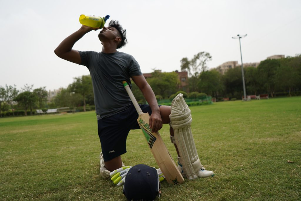 A cricket player hydrates after a workout