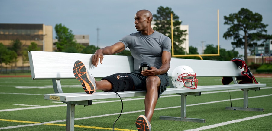Football player sitting on bench while using PowerPlay knee compression wrap.