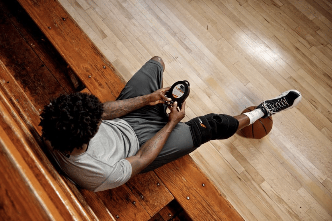 A basketball player uses a PowerPlay standard knee wrap for sideline cold compression therapy.
